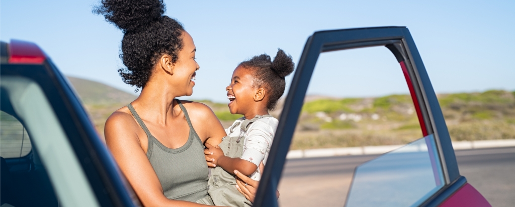 woman holding young child outside of vehicle